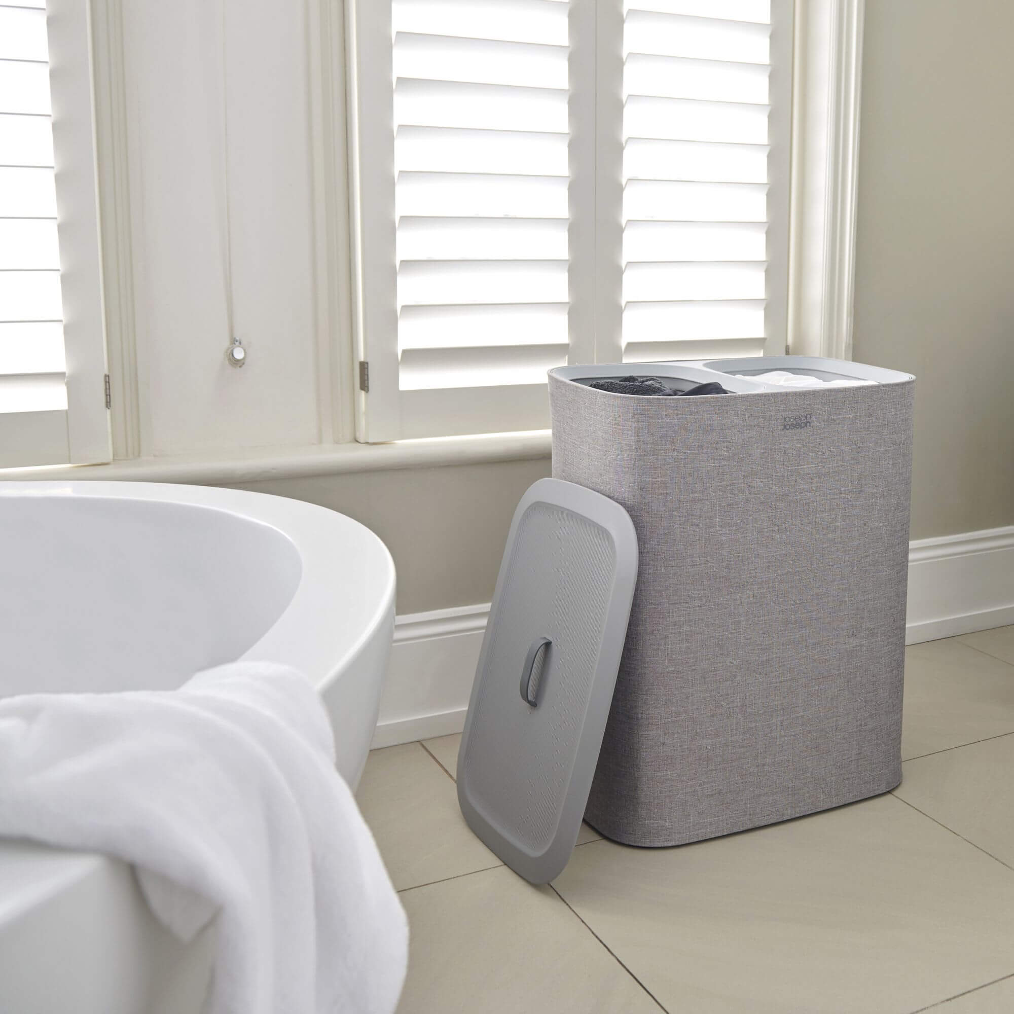 Joseph Joseph Tota Twin Laundry Hamper next to a bathtub with clothes inside