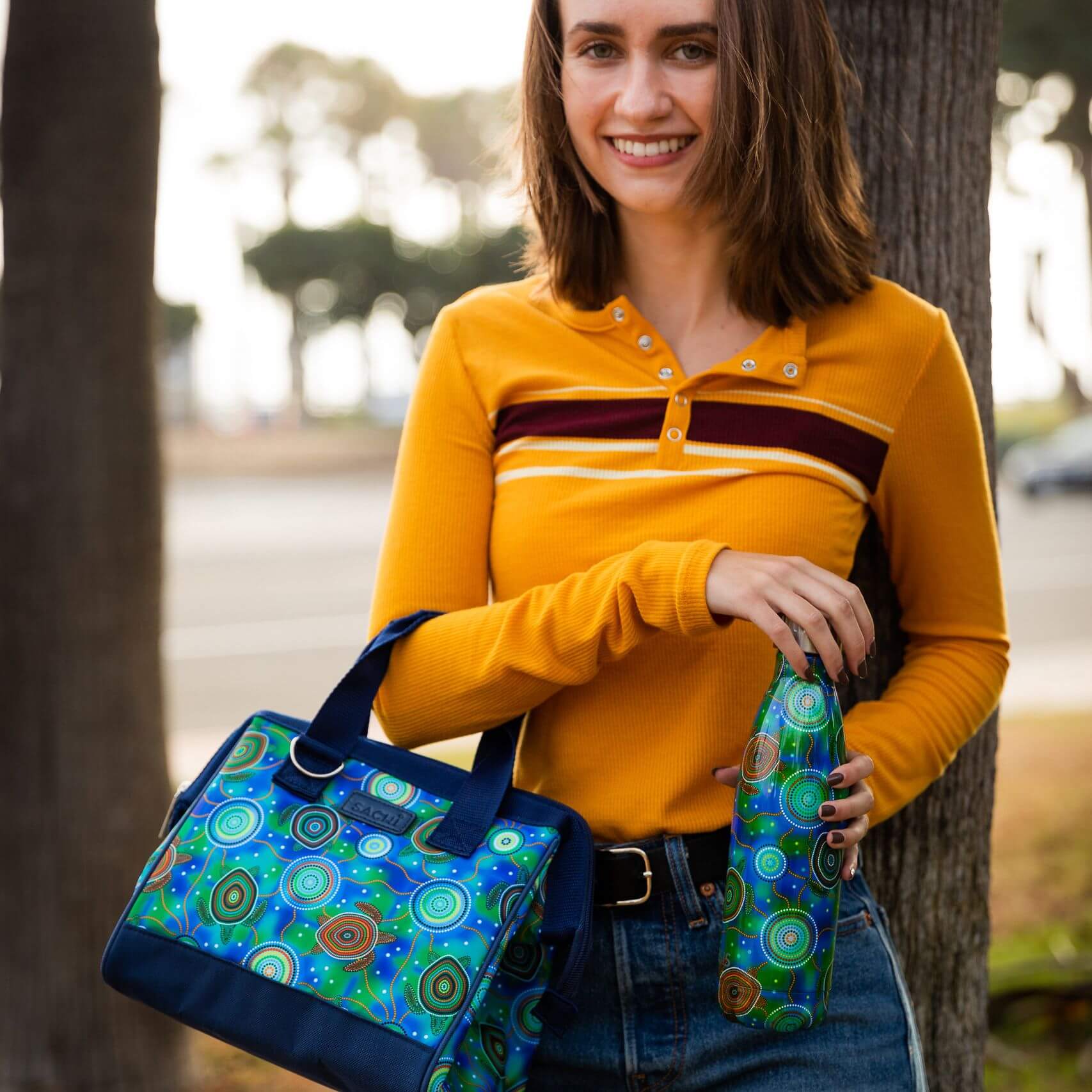 A woman holding a patterned lunch bag and insulated water bottle